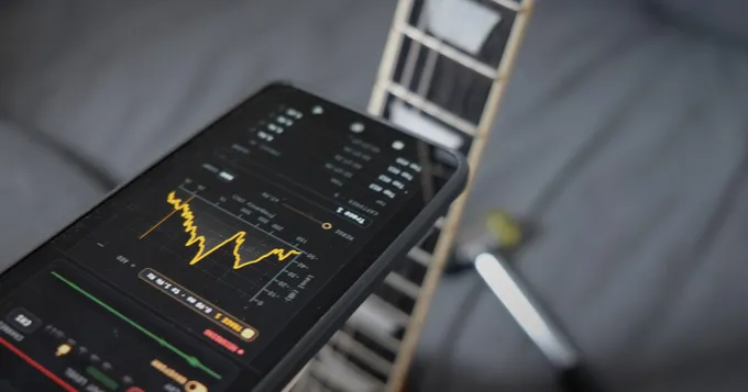 A phone running Fretoscope's tap spectrum held next to a guitar neck, with a small hammer in the background.