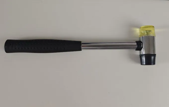 A small fret hammer with a black rubber face and a clear yellow plastic face on a steel handle with a rubber grip