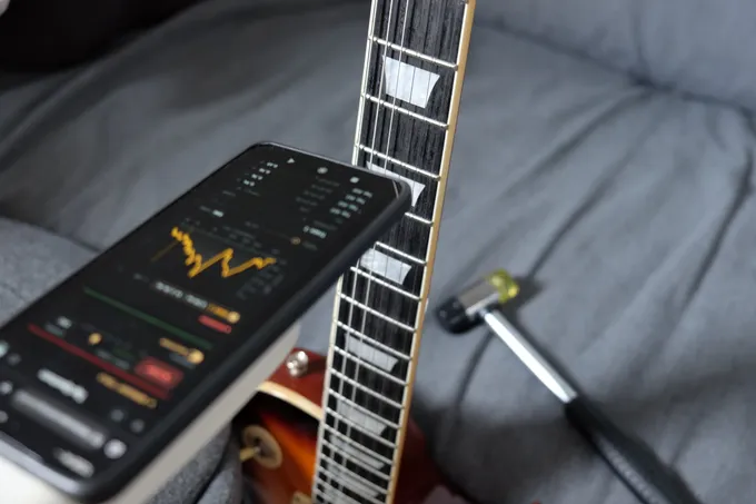 The tap test on the SC-450: the guitar held upright by its body with the neck free, a phone running Fretoscope’s Tap Spectrum held close to the fretboard, and the hammer used for the knocks lying beside it